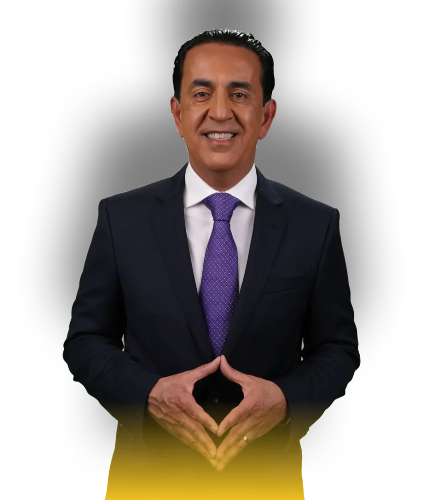 A man in a dark suit, white shirt, and purple tie stands smiling with his hands clasped in front of him. The background is white with a soft shadow, and there is a yellow gradient at the bottom of the image.