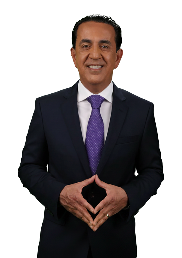 A man in a dark suit, white shirt, and purple tie stands smiling with his hands forming a triangle shape in front of him, exuding confidence like el mero mero. The background is plain white.